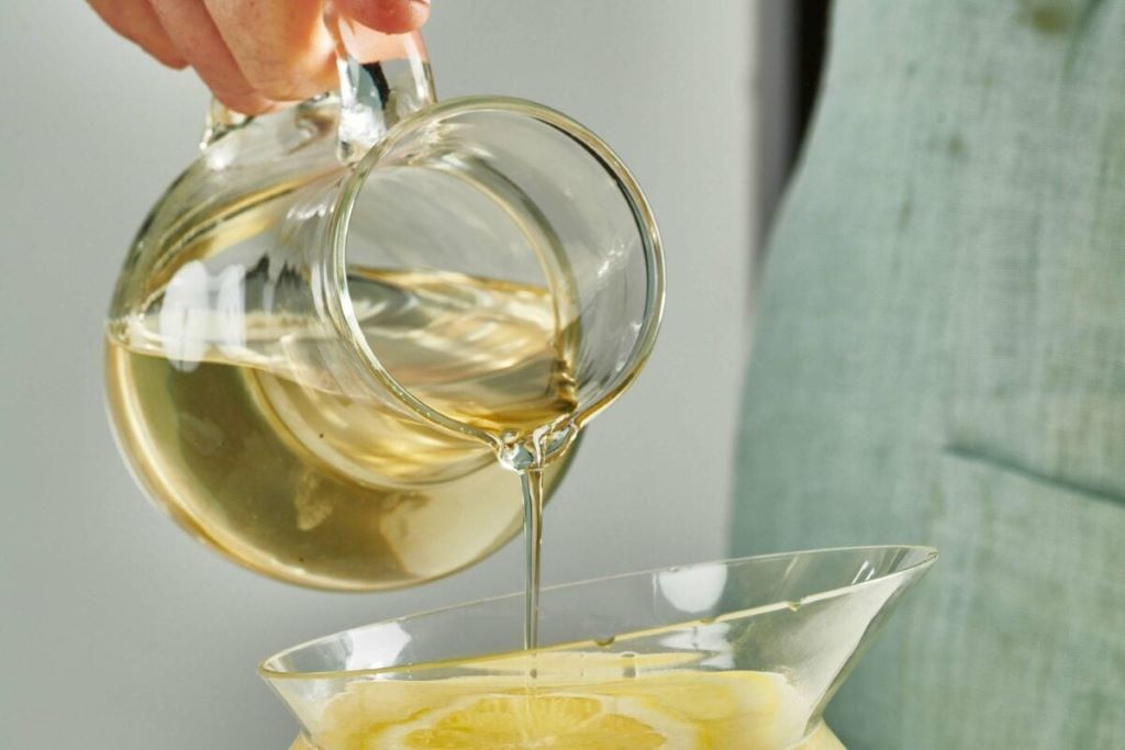 A hand pouring allulose simple syrup from a bottle into a glass of iced coffee