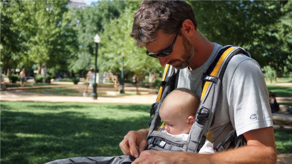 Dad doing quick diaper change in park with baby safely in front carrier, hands free